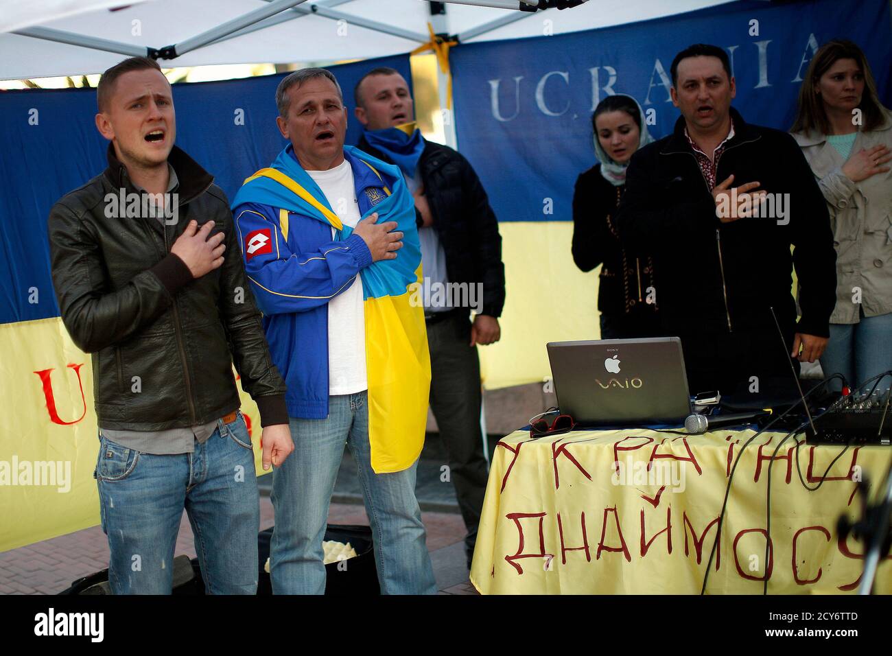 Ukrainians living in Malaga sing the Ukrainian anthem during a protest against Russian President Vladimir Putin and in favor of unity and democratic freedom in Ukraine, in downtown Malaga, southern Spain, March 16, 2014. France on Sunday demanded Russia immediately take measures to reduce 'pointless and dangerous' tensions in Ukraine, calling the secession referendum held in the Crimea region illegal. The words on the Ukrainian flag (bottom R) reads, 'Ukrainians united'. REUTERS/Jon Nazca (SPAIN - Tags: POLITICS CIVIL UNREST ELECTIONS) Stock Photo