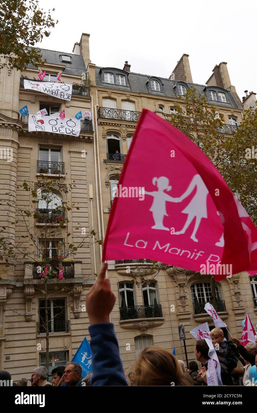 Demonstrators walk past a building where a woman stands on her balcony  which is covered with banners in support of kid's rights to a mother and  father as tens of thousands of