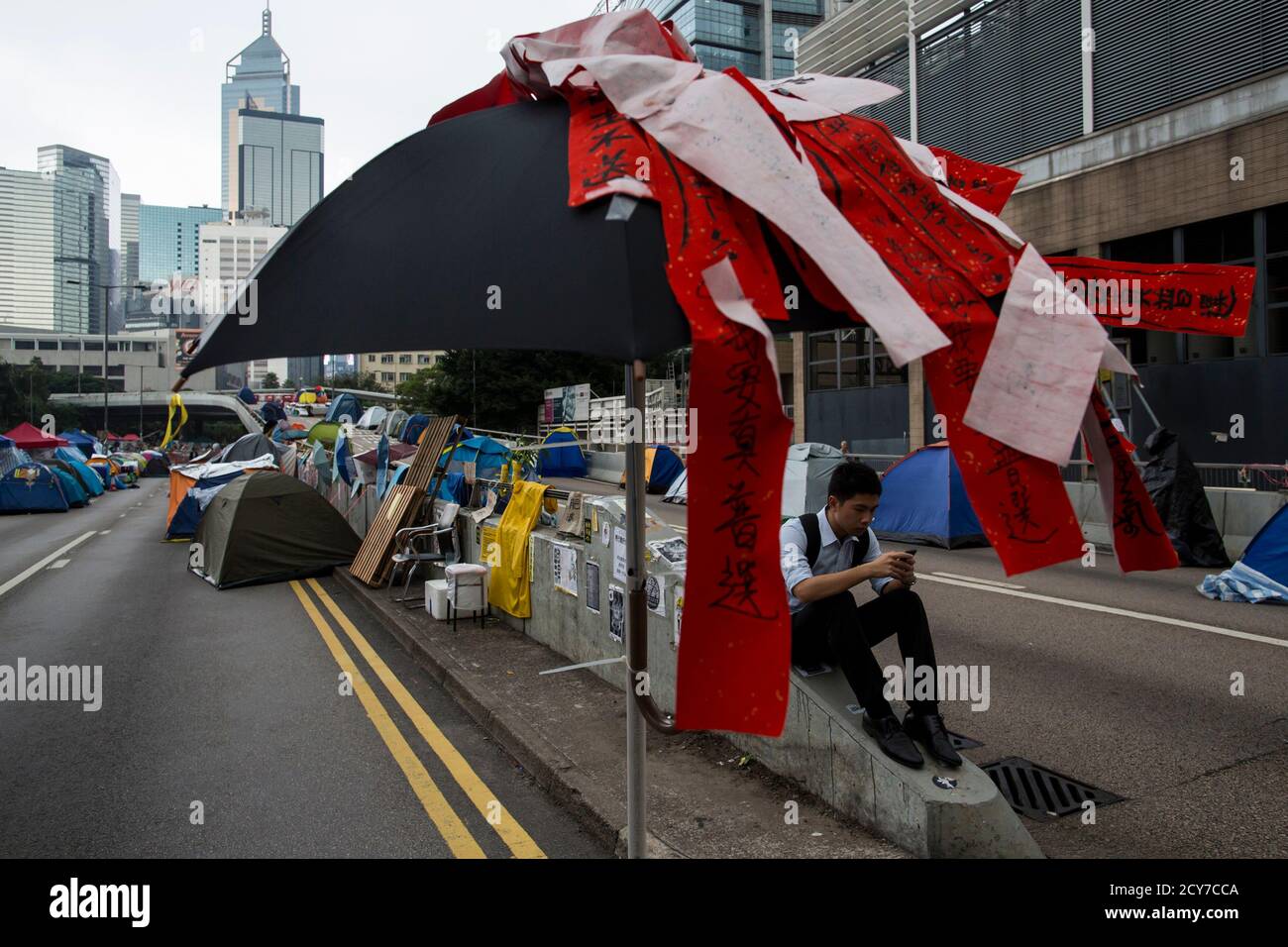 A pro-democracy protester sits on a divider next to an umbrella with protest messages, reading 'We want universal suffrage', in an occupied area outside the government headquarters in Hong Kong November 12, 2014. Hong Kong's acting chief executive on Tuesday called on pro-democracy protesters to clear sites they have occupied for more than six weeks and warned holdouts they could face arrest, a move that could swell protest numbers.   REUTERS/Tyrone Siu (CHINA - Tags: POLITICS CIVIL UNREST) Stock Photo