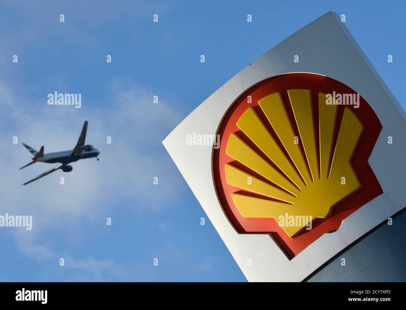 A passenger plane flies over a Shell logo at a petrol station in west  London, January 29, 2015. Royal Dutch Shell blamed writedowns and forex  losses for making almost no money in