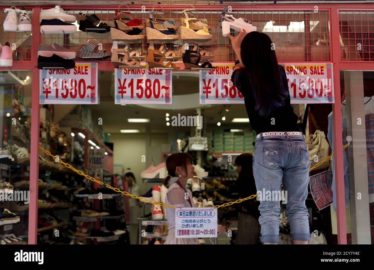A shops clerk displays a shoe atop price tags as she prepares to open a  shoes store at Tokyo's Harajuku shopping district, Japan, April 30, 2015.  The Bank of Japan maintained its