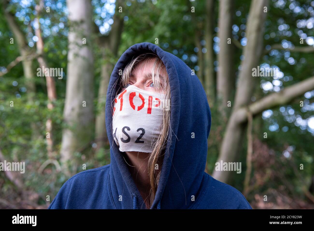 Wendover, UK. 1st October, 2020. A protester wears a Stop HS2 facemask as she watches the tree house evictions. Peaceful tree protectors and environmental campaigners at the Stop HS2 Jones Hill Protection Camp were being evicted today from their homes in the trees by the National Eviction Team Enforcement Agents working on behalf of HS2 Ltd. The over budget and controversial HS2 High Speed Rail link from London to Birmingham project puts 108 ancient woodlands, 693 wildlife sites and 33 SSSIs at risk of damage or destruction. Maureen McLean/Alamy Live News Stock Photo