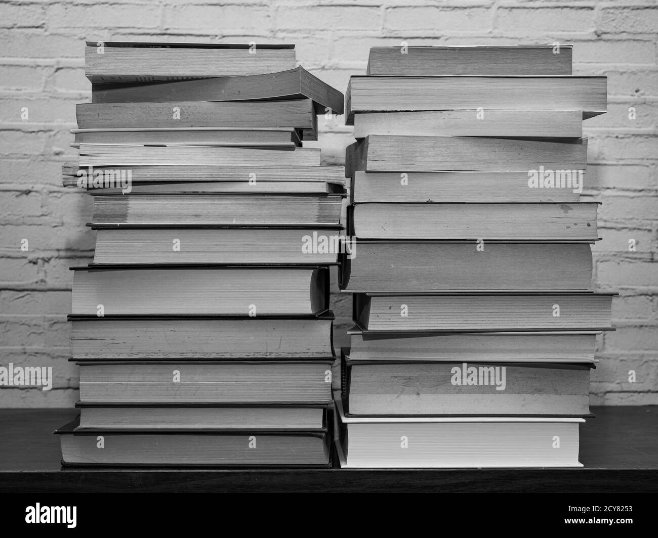 Black and white image of some books stacked on a shelf, light brick background Stock Photo