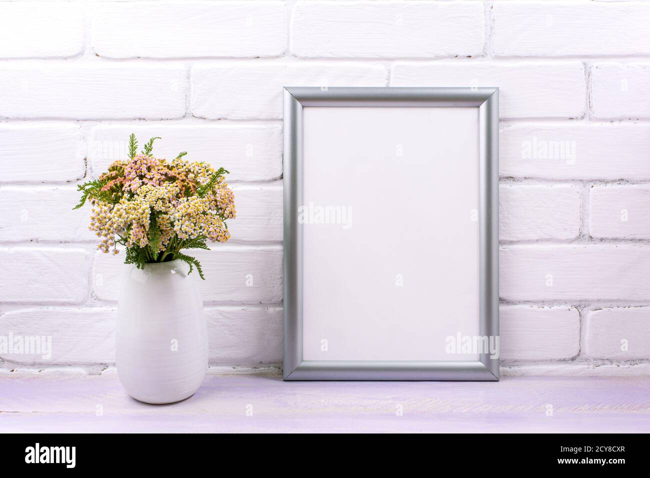 Silver frame mockup with pink yarrow wildflowers in the vase. Empty frame mock up for presentation artwork. Template framing for modern art. Stock Photo