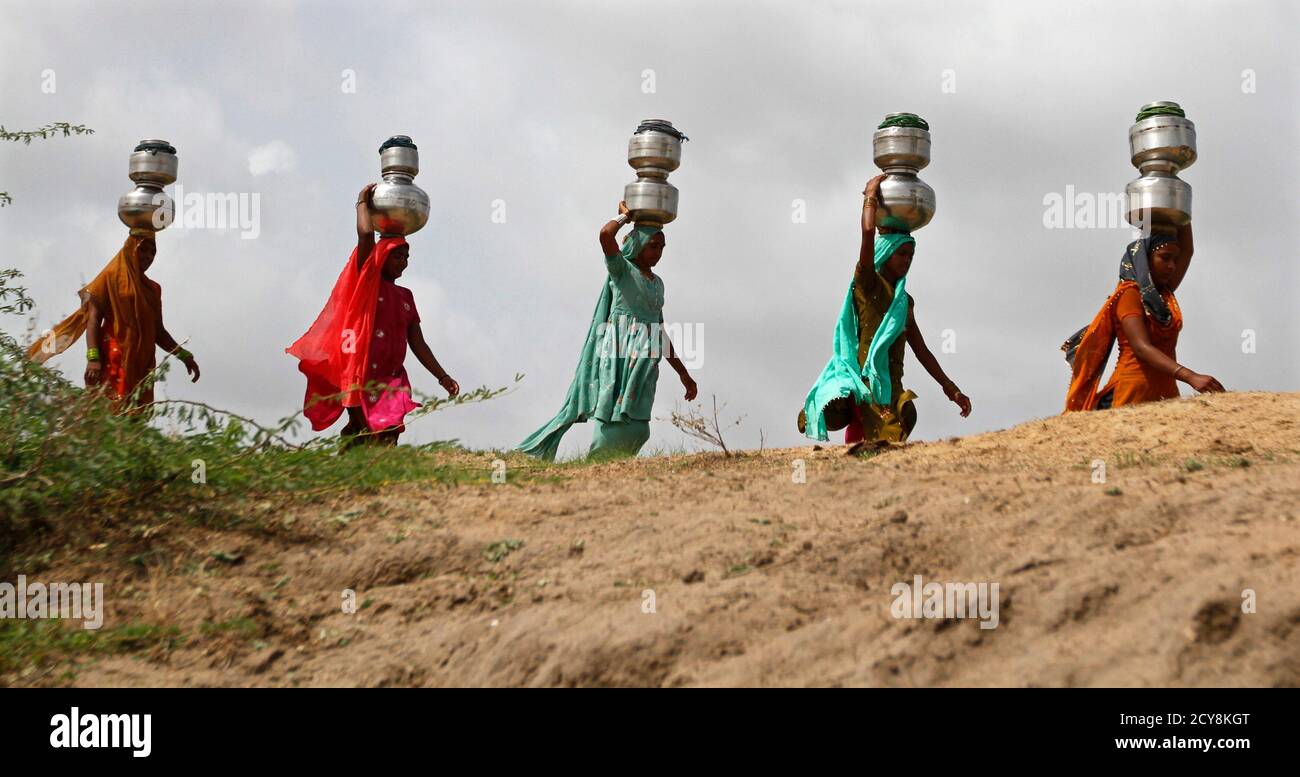 Women walk carrying metal pitchers filled with drinking water to their  homes against the backdrop of pre-monsoon clouds at Nani Shinoli village in  the western Indian state of Gujarat June 24, 2012.
