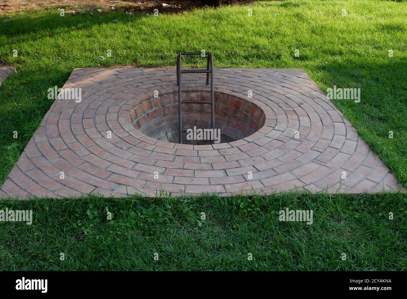 Manhole with ladder in garden.  (Not a real manhole, designed in garden as an artistic object) Stock Photo