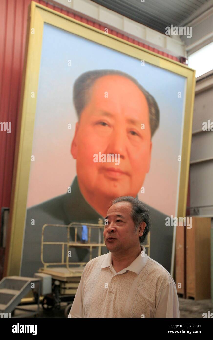Ge Xiaoguang speaks in front of a giant portrait of China's late Chairman Mao Zedong during a interview with Reuters in his working studio located between the Tiananmen Square and the Forbidden City in Beijing June 29, 2011. Reclusive Chinese painter Ge's art has gazed over one of the world's most famous city squares for decades. For 30 years, he has painted the portraits of former paramount leader Mao Zedong that look across Beijing's Tiananmen Square. The giant oil paintings of the "Great Helmsman" have kept watch from the Gate of Heavenly Peace since the Communist Party won the civil war an Stock Photo