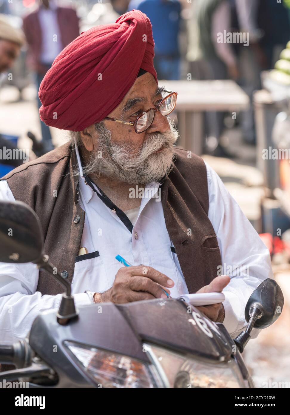 New Delhi, India - February 19, 2018 - Man With Grey Beard and Turban Writes In His Notebook While Talking To Person Off Screen Stock Photo