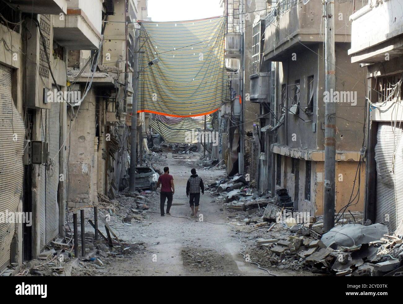 Men walk on rubble of damaged buildings, near curtains erected as protection from snipers loyal to Syria's President Bashar al-Assad, in Juret al-Shayah in Homs November 1, 2012. Picture taken November 1, 2012.  REUTERS/Yazan Homsy (SYRIA - Tags: CONFLICT POLITICS) Stock Photo