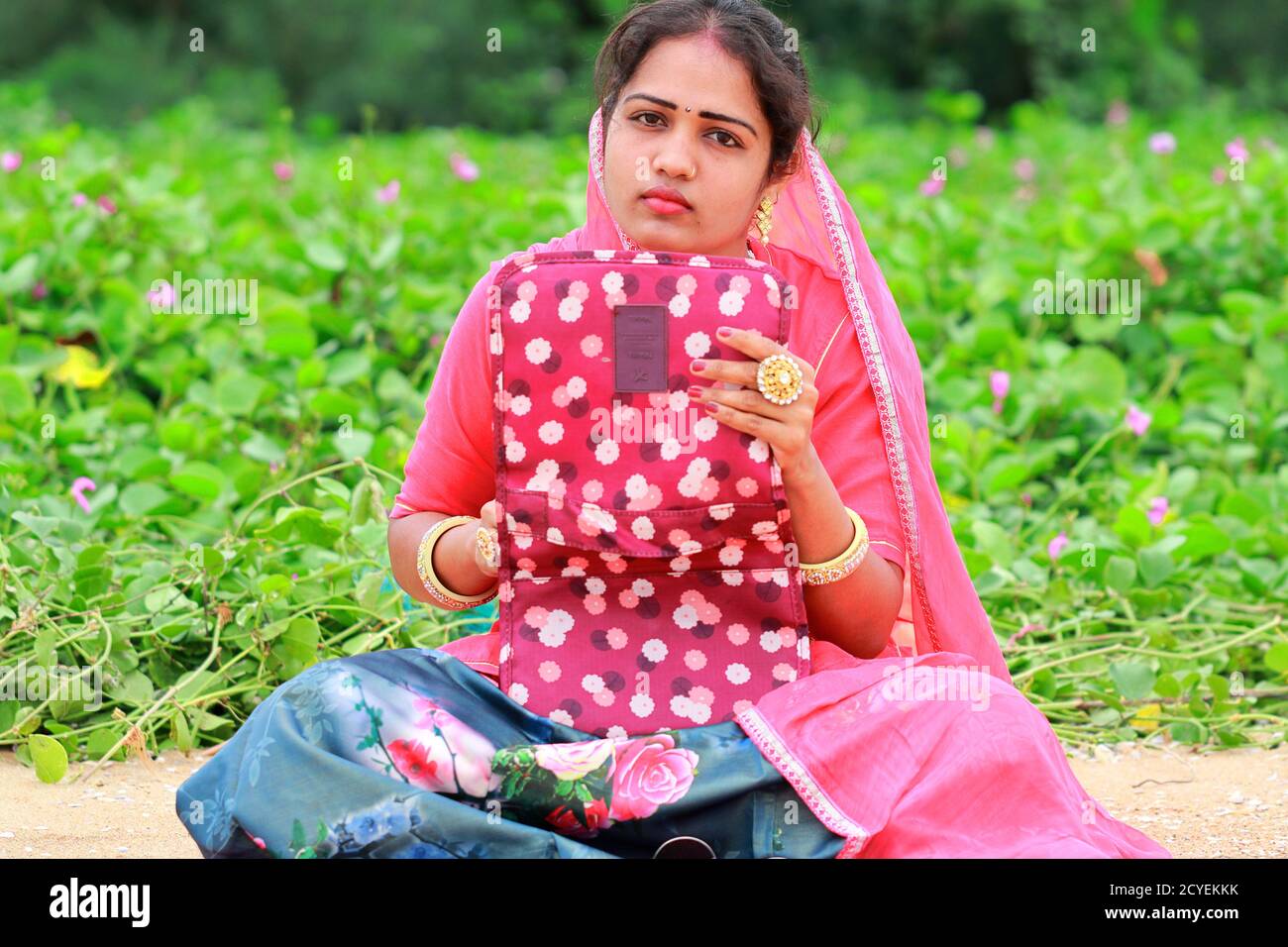 A young Indian fashion artist woman sitting in the garden, holding the Wallet bag in her hand and looking at the camera, thinking about the solution Stock Photo