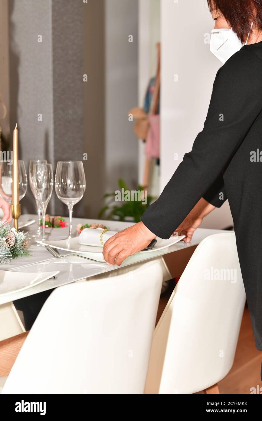 Asian Woman With A Face Mask Arranging A Table With Christmas Decorations Glasses And Plates Christmas Celebration And Safety Concept Stock Photo Alamy