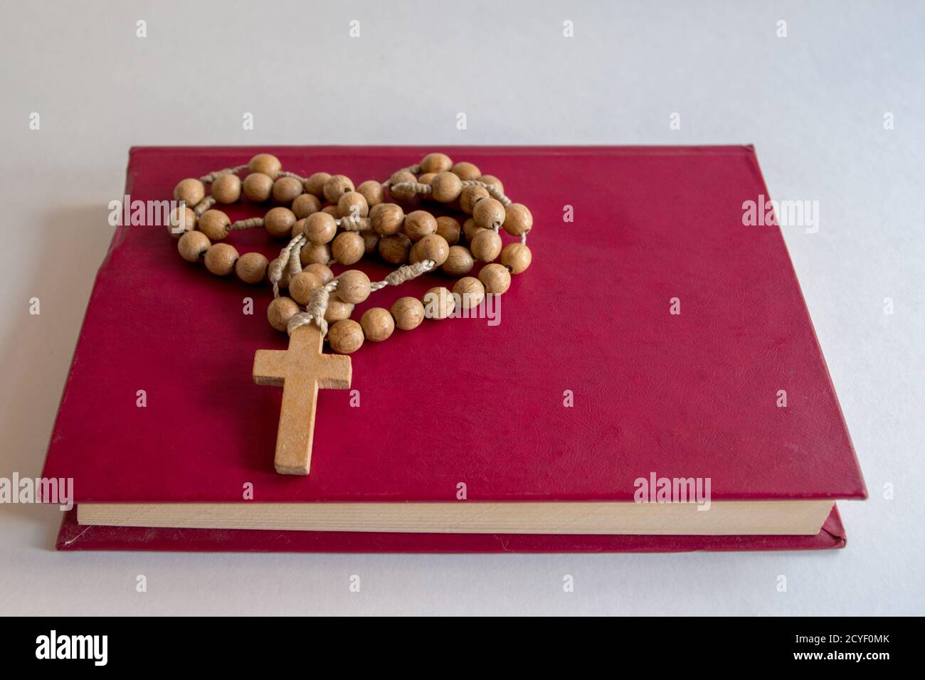 Small prayer book in pink leather cover lying with ends of pages forward with Catholic wooden rosary with cross on it folded in form of heart. Stock Photo