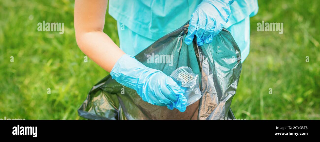 Child collects plastic trash from grass throwing garbage in garbage bag