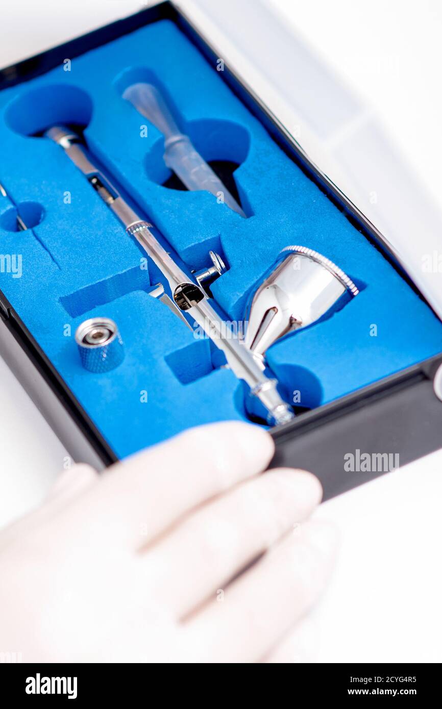 Close up shot of manicure master hand is taking out new clean airbrush tool for nails wearing gloves from the blue box Stock Photo
