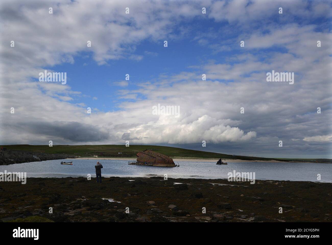 A man takes a photograph of a blockship in the Orkney Islands, Scotland May 8, 2014. A blockship is a boat that has been sunk in order to block a waterway. During both World Wars, Scapa Flow was an important British naval base, and the site of significant loss of life. Following the end of World War One, 74 German warships were interned there, and on June 21, 1919 most were deliberately sunk, or scuttled, at the orders of German Rear Admiral Ludwig Von Reuter, who mistakenly thought that the Armistice had broken down and wanted to prevent the British from using the ships. Now Scapa Flow is a p Stock Photo