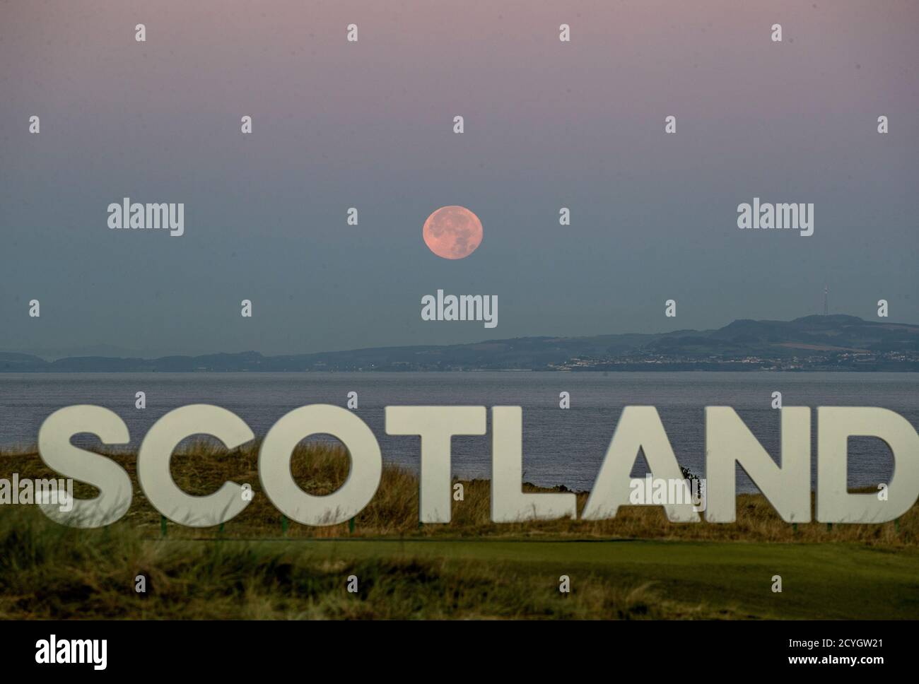 The Moon, known as a Harvest Moon during the month of October, sets behind a sign that reads 'SCOTLAND' on The Renaissance Club Golf course at North Berwick. Stock Photo