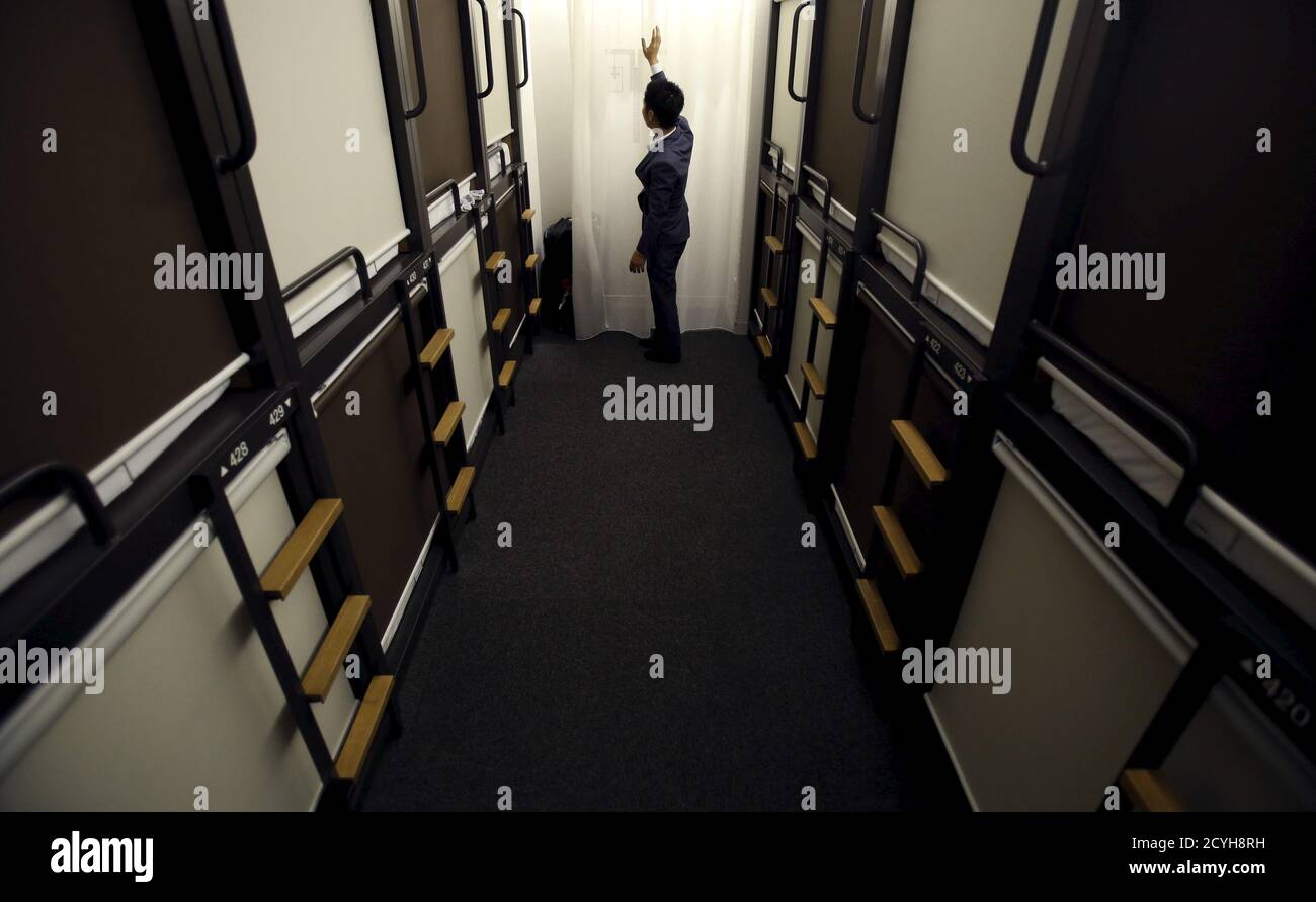 A hotel staff member touches a curtain in a corridor between one man  capsule bed units called "pods" inside a hotel at Grids at the Akihabara  shopping district in Tokyo, Japan, May