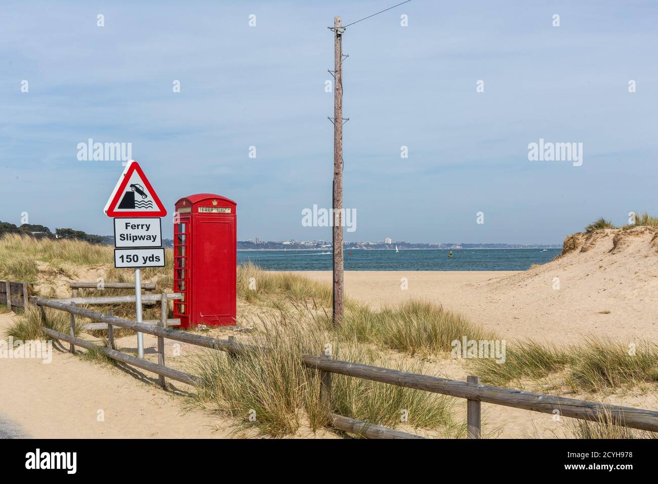 A telegraph pole, phone box and a sign saying 150 years to the ferry slipway nestle in the sand dunes on the slip road to the car ferry across Poole H Stock Photo