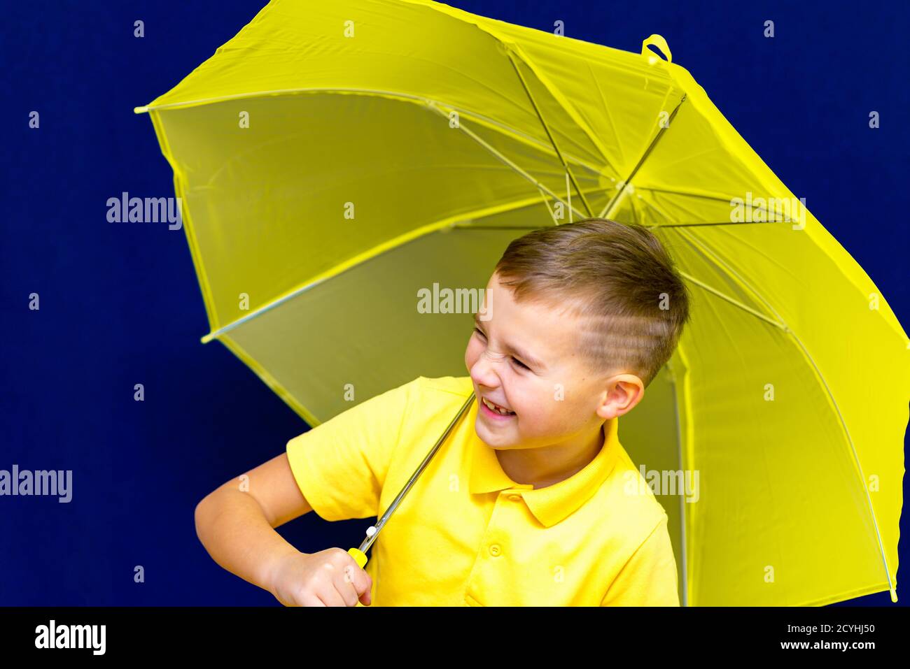 Side view Attractive caucasian blond schoolboy with umbrella on blue