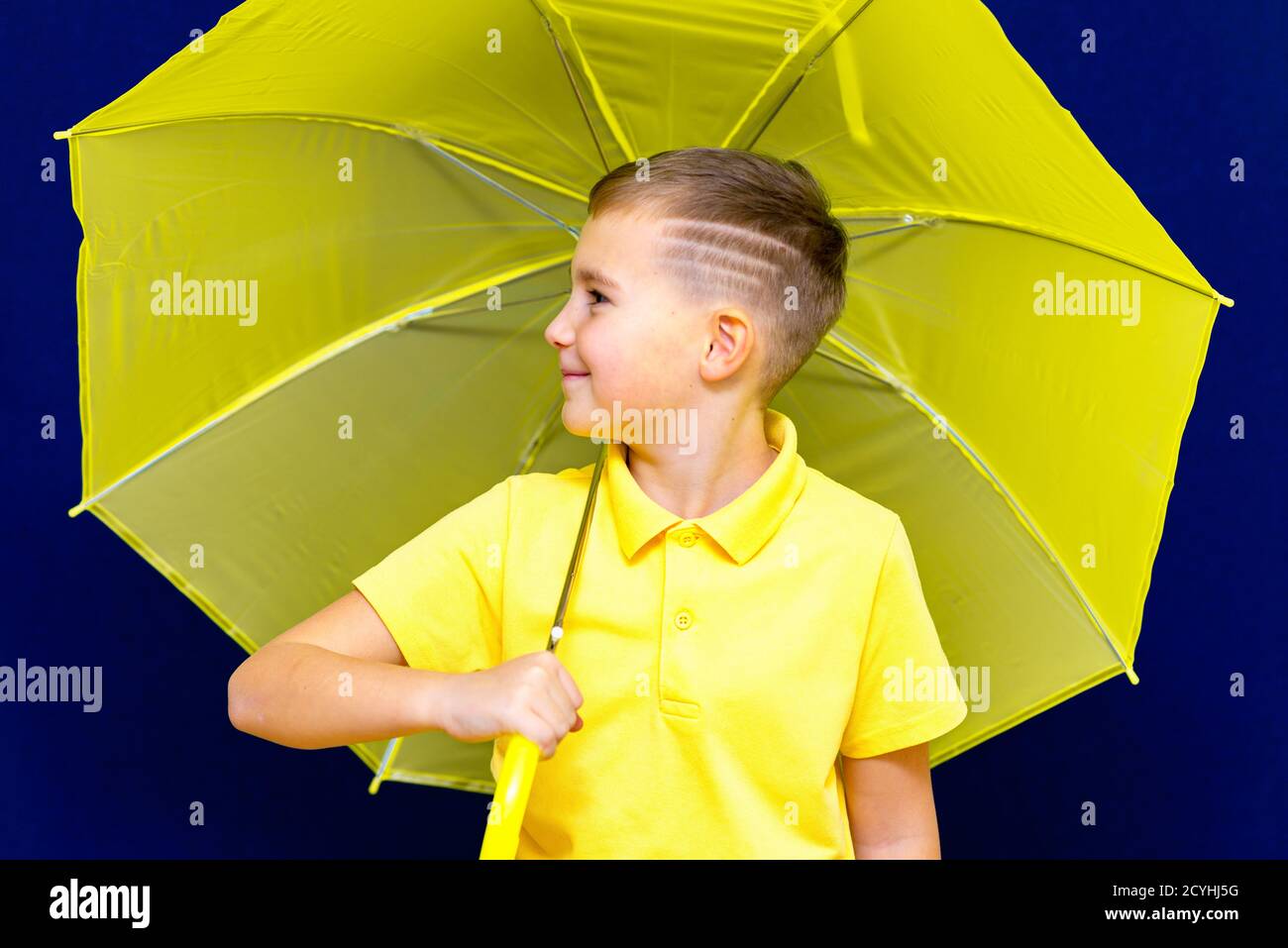 Side view Attractive caucasian blond schoolboy with umbrella on blue