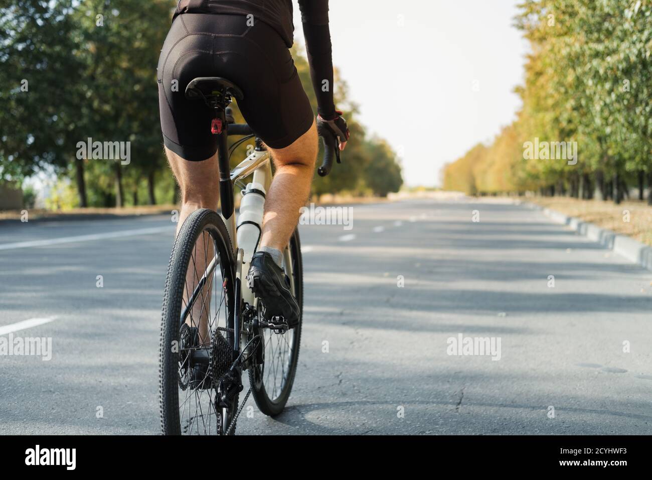 Man on a gravel bike on the road, back view. Legs of a cyclist riding a