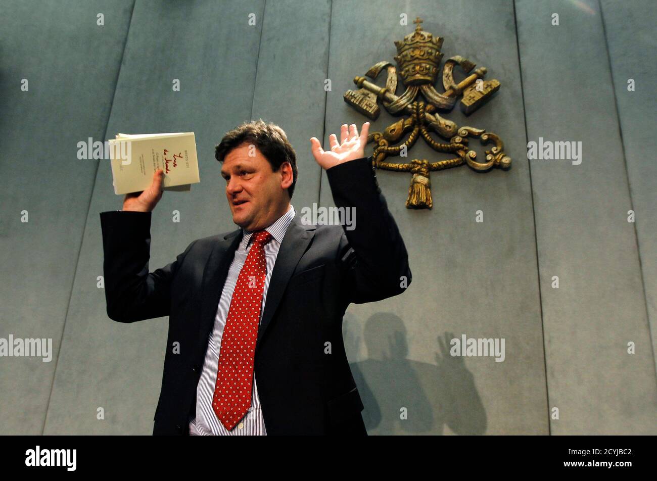 German Catholic journalist Peter Seewald reacts as he holds his new book about Pope Benedict XVI while leaving at the end of a news conference at the Vatican November 23, 2010. Pope Benedict says in the new book, called 'Light of the World: The Pope, the Church, and the Sign of the Times', that he would not hesitate to become the first pontiff to resign willingly in more than 700 years if he felt himself no longer able, 'physically, psychologically and spiritually', to lead the church. The book, an interview with German Catholic journalist Peter Seewald, has so far made headlines for the pope' Stock Photo