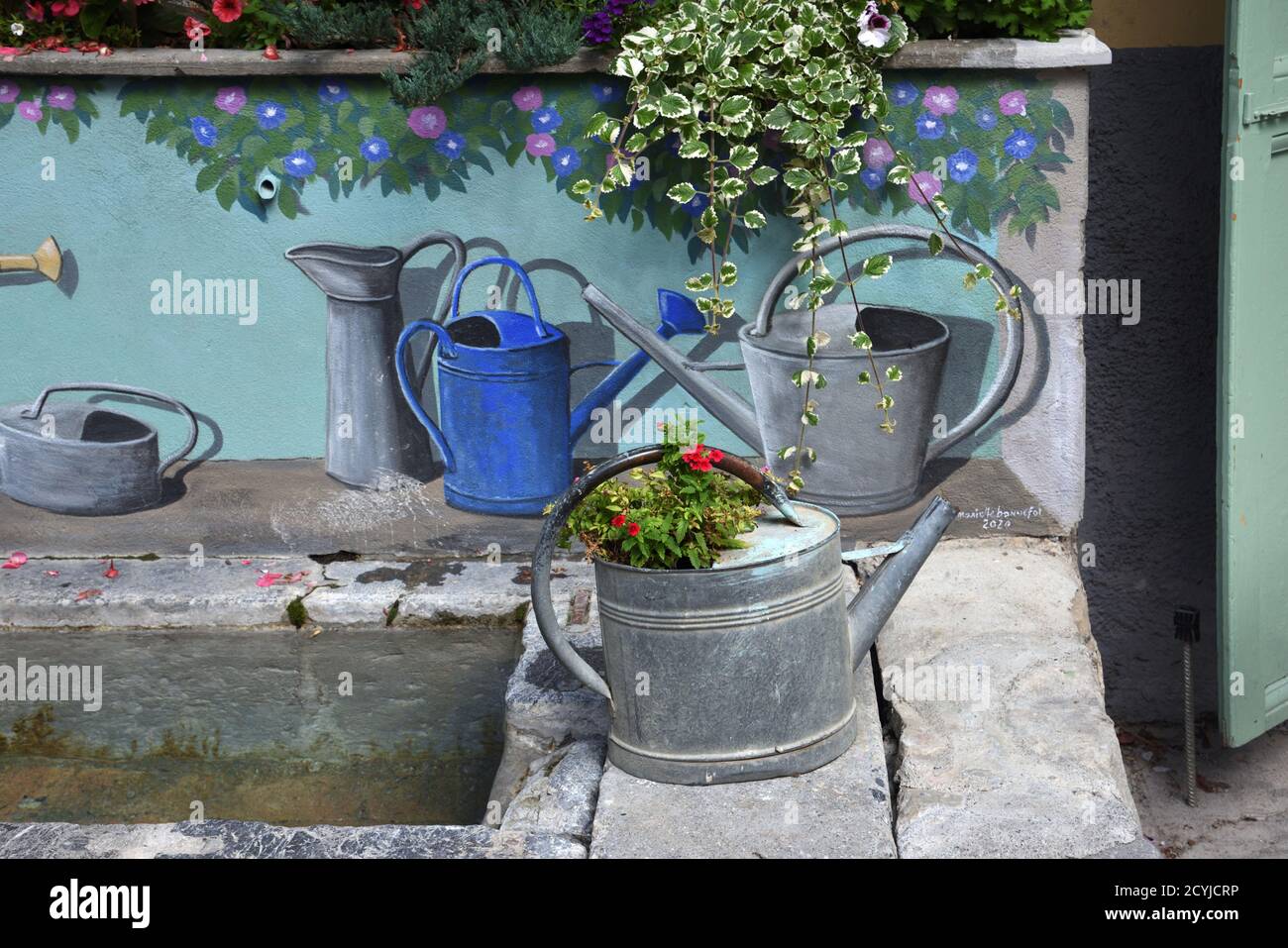 Vintage or Old Metal Watering Can & Painted Watering Cans Decorating Village Fountain or Street Fountain Colmars-les-Alpes Provence France Stock Photo
