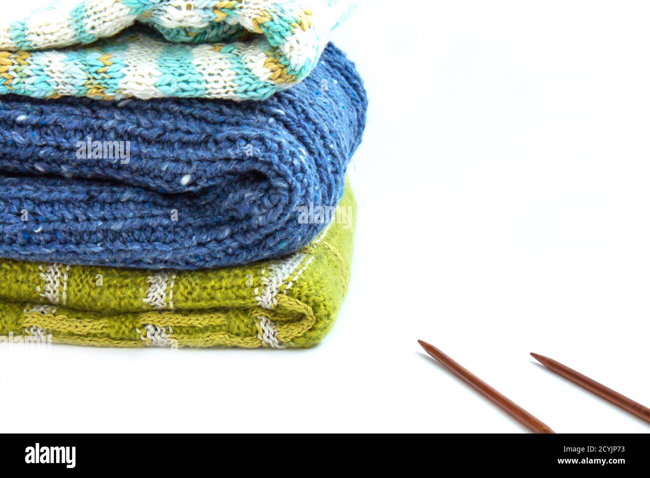 Stack of blue, brown, green knitted sweaters and knitting needles on a white background. Home comfort. Casual wear. Autumn mood. Concept of autumn tid Stock Photo