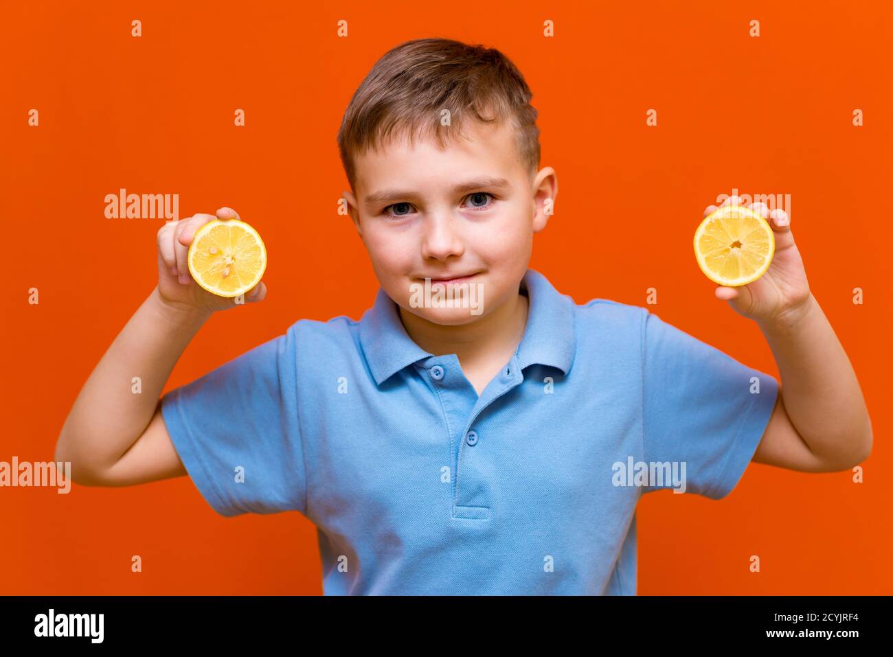 Close up Caucasian young child shows raw slices of lemon on a orange background. Healthy, lifestyle and a happy childhood concept. Stock Photo