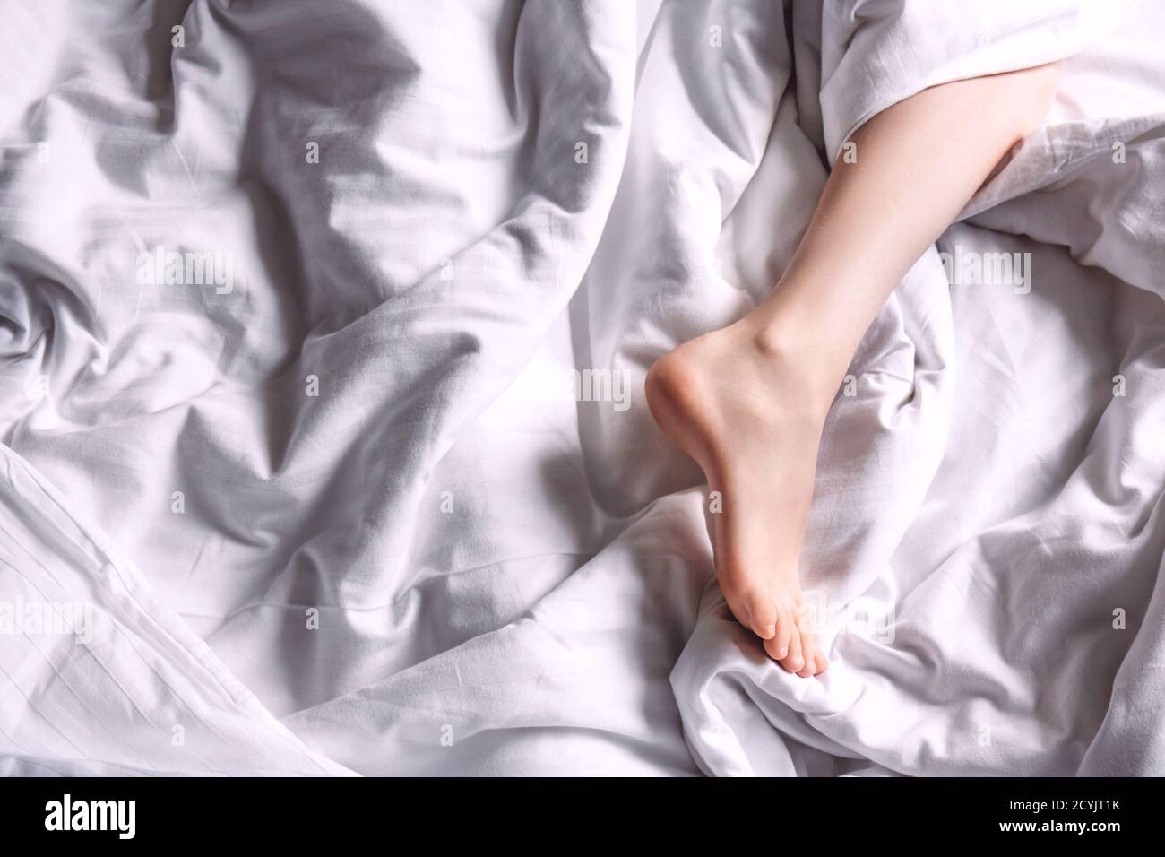 Beautiful female leg on white bedding in the sun. Selective focus. Close up Stock Photo