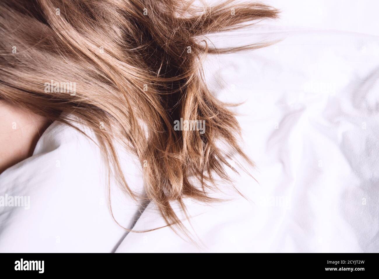 Beautiful, blonde, long female hair on a snow-white bed in the sun. Selective focus. Close up Stock Photo