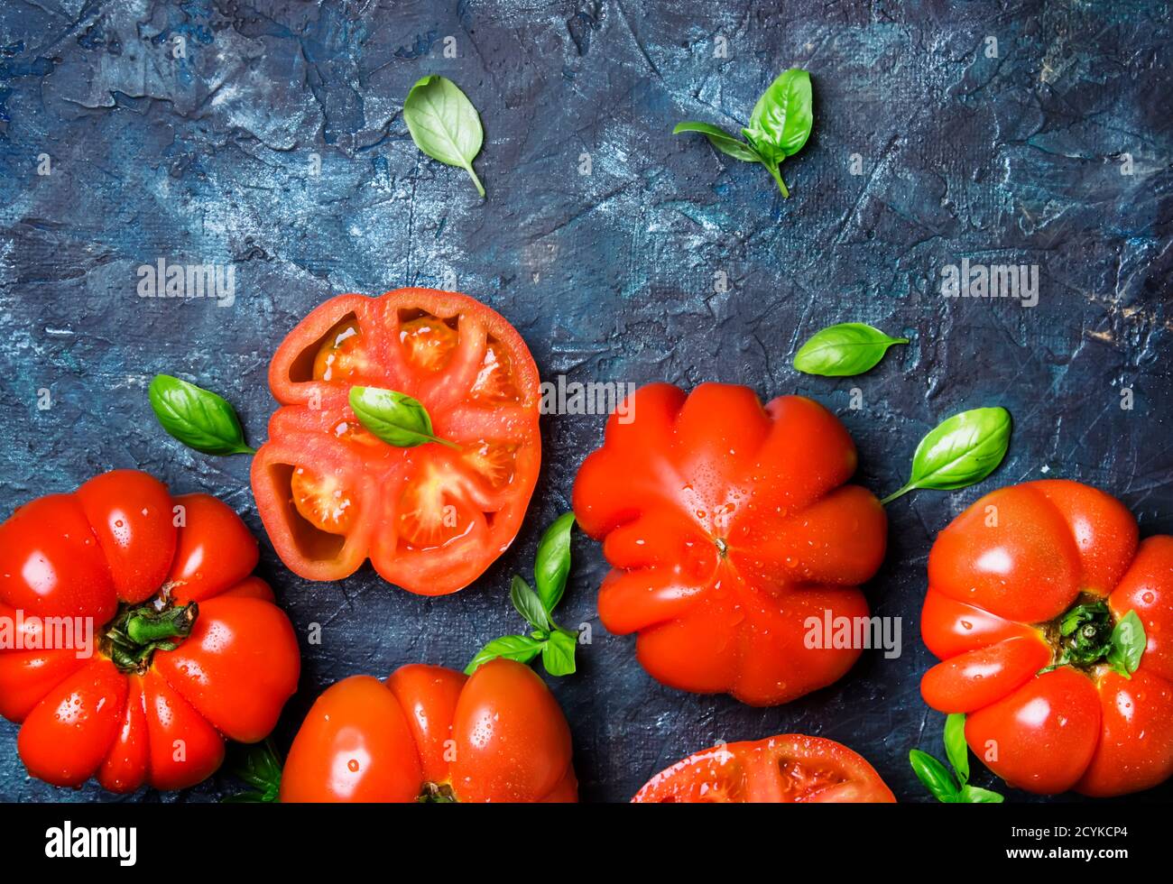 Red tomatoes with basil leaves on the black stone background, top view ...