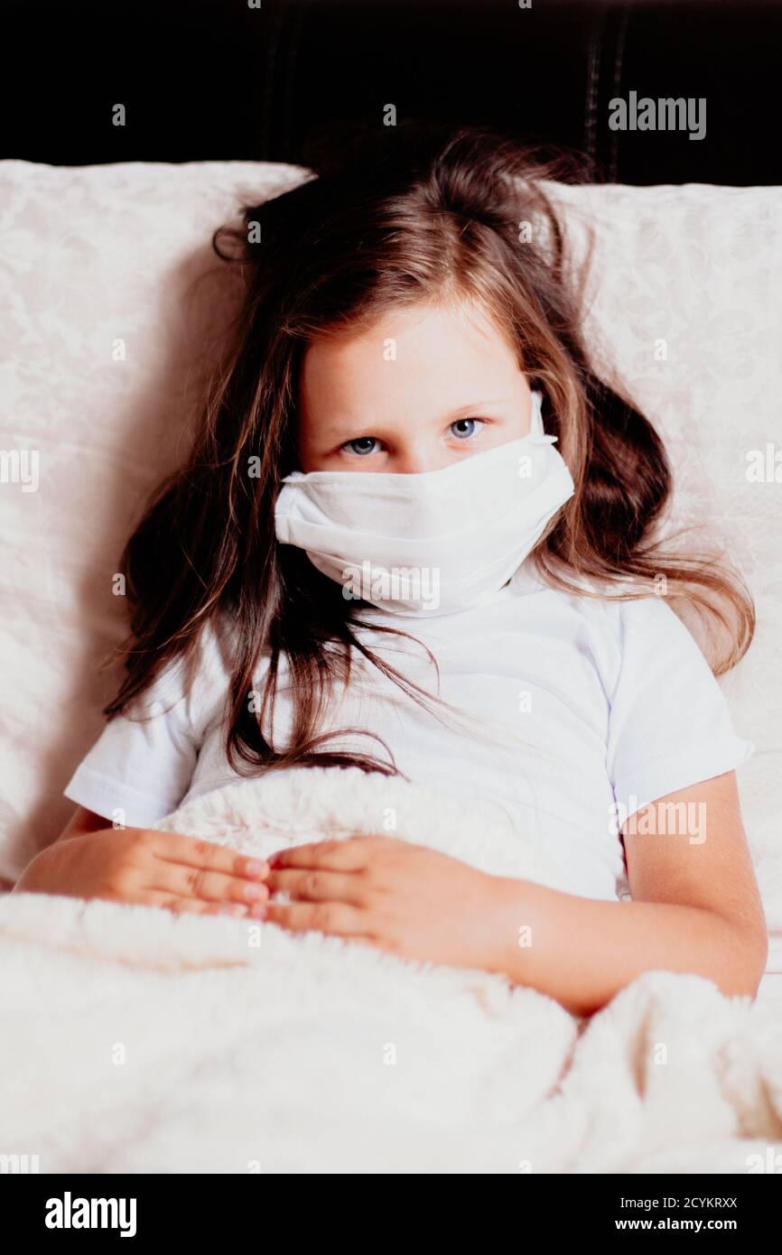 girl close-up sitting in a white mask on the bed in the bedroom, self-isolation with a cold, the second wave of viruses Stock Photo