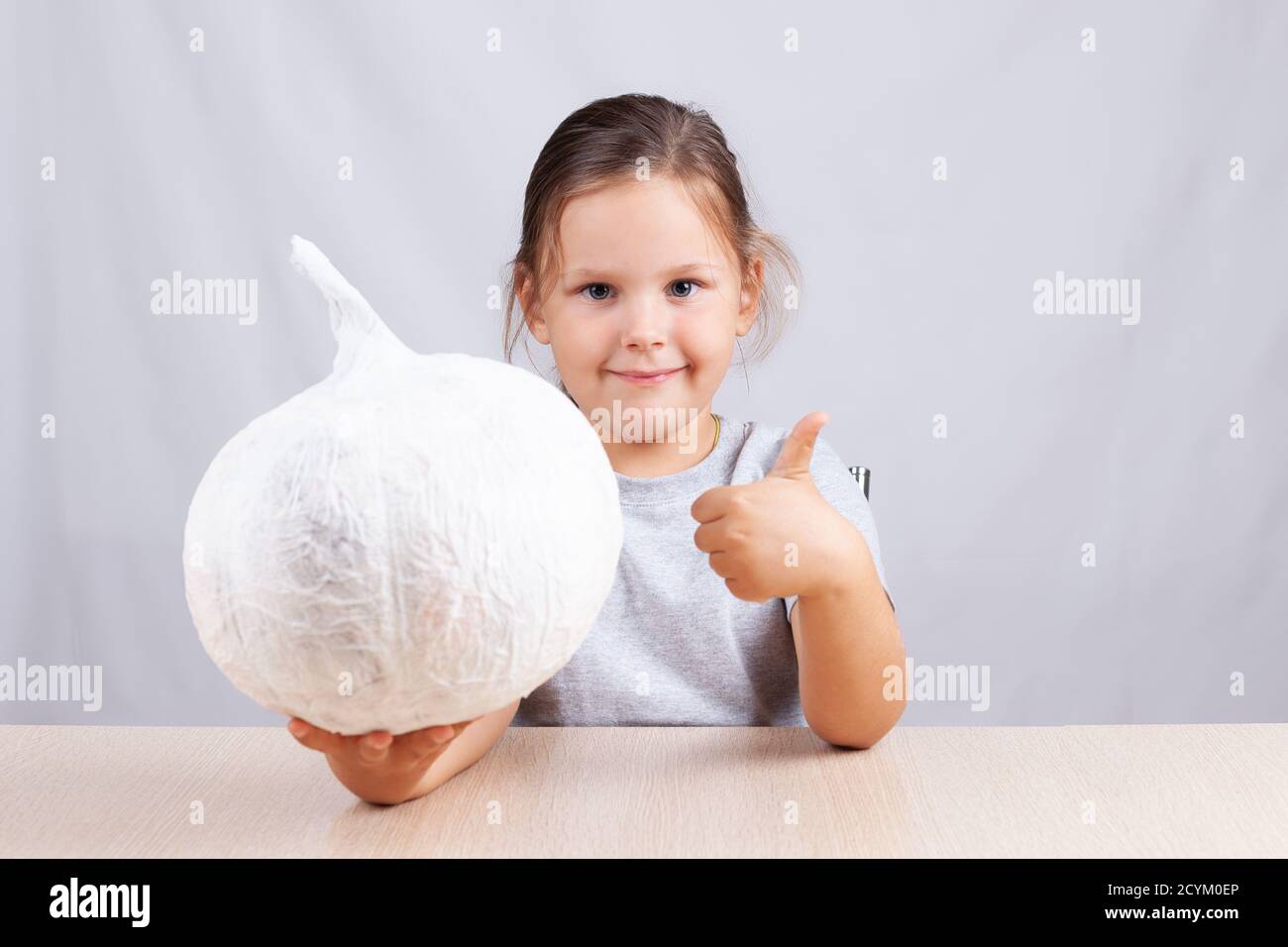 the child shows the thumbs up and holding a homemade pumpkin napkins and paper decorations for Halloween Stock Photo
