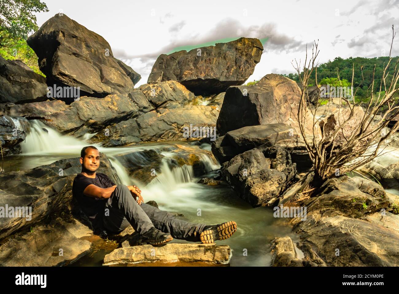 man relaxing at rock with the beautiful waterfall stream long exposure shot at evening image is taken at remote western ghat forests karnataka india. Stock Photo