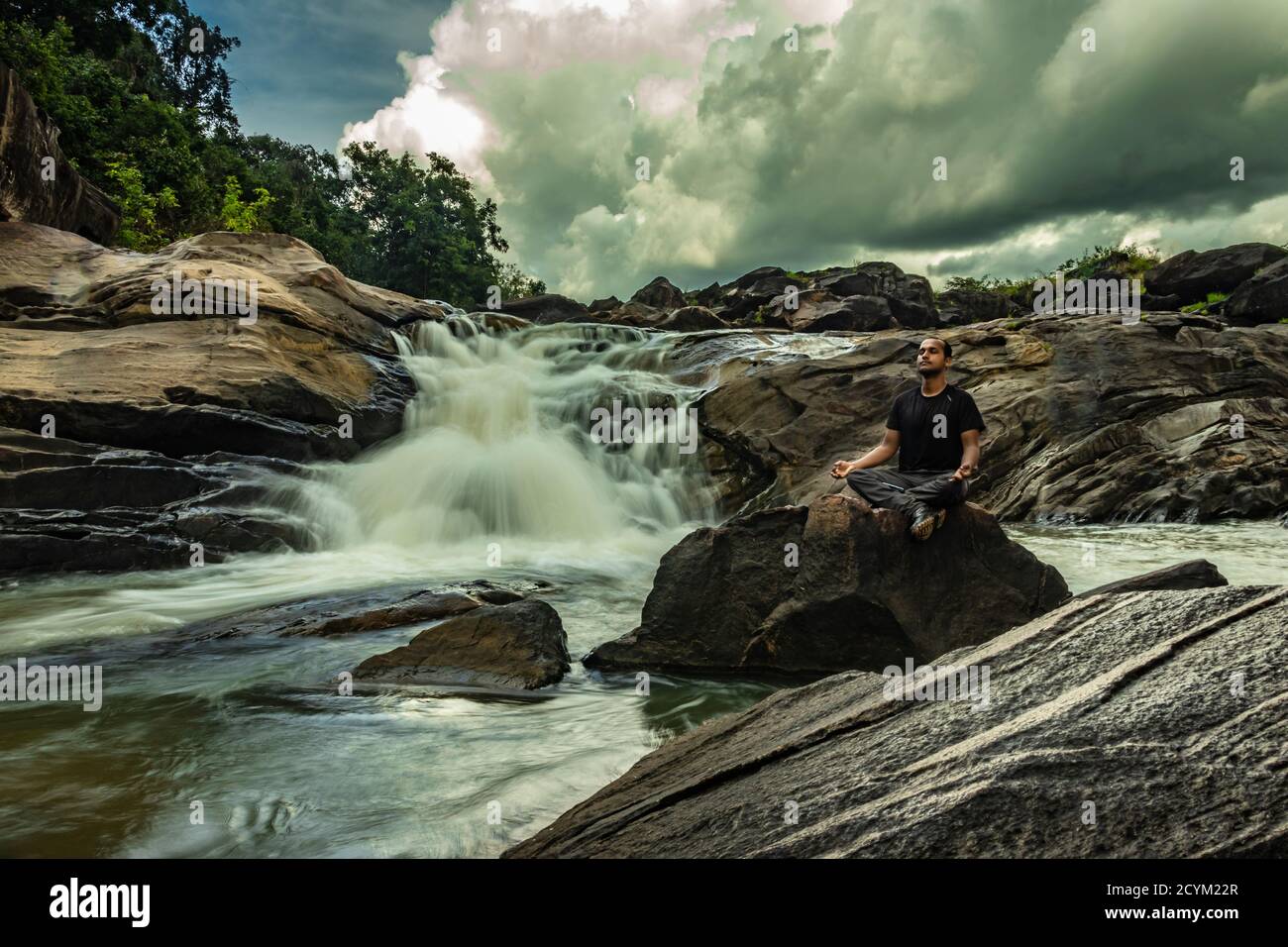man meditating at rock with the beautiful waterfall stream at evening image is taken at remote western ghat forests karnataka india. it is showing the Stock Photo