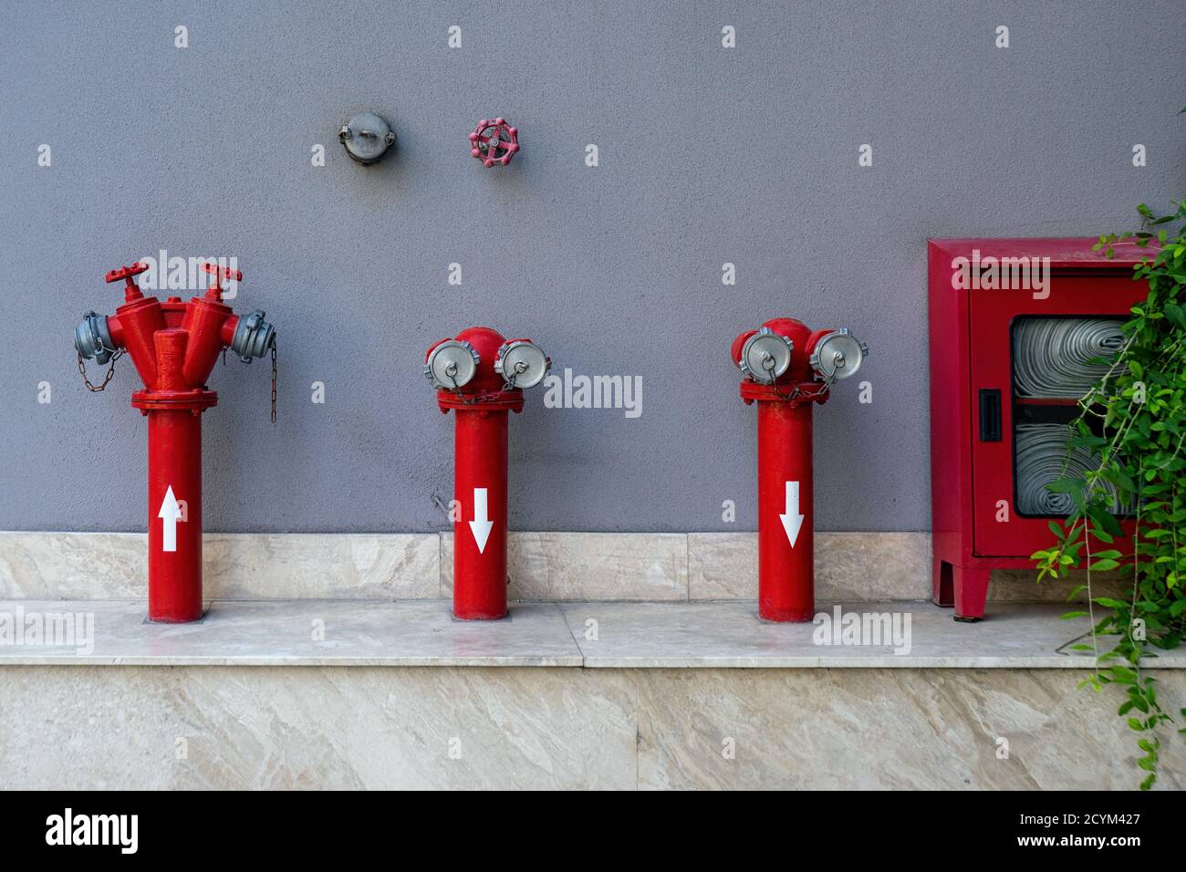 Set of different red fire hydrants outside at gray wall.  Fire safety corner with the necessary extinguisher equipment. Stock Photo