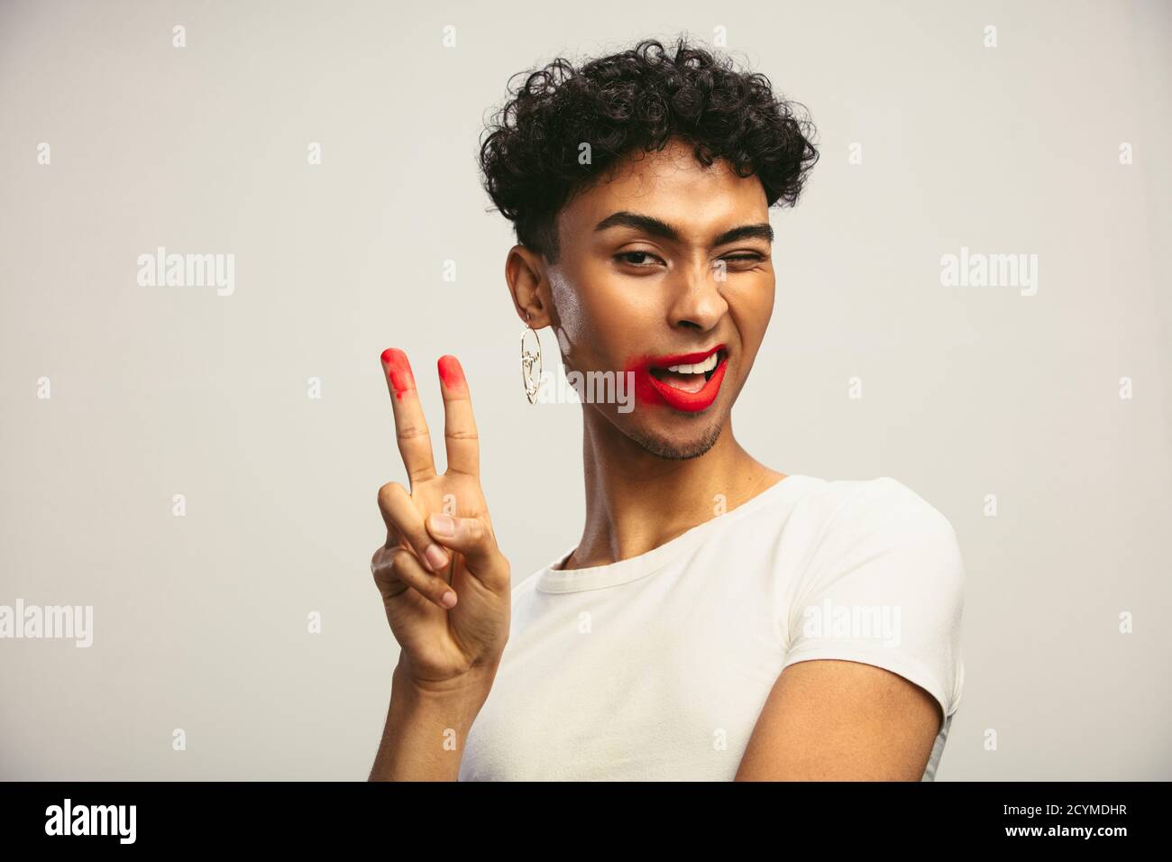 Androgynous man with smeared lipstick showing peace sign. Transgender male with smudges lipstick looking at camera. Stock Photo