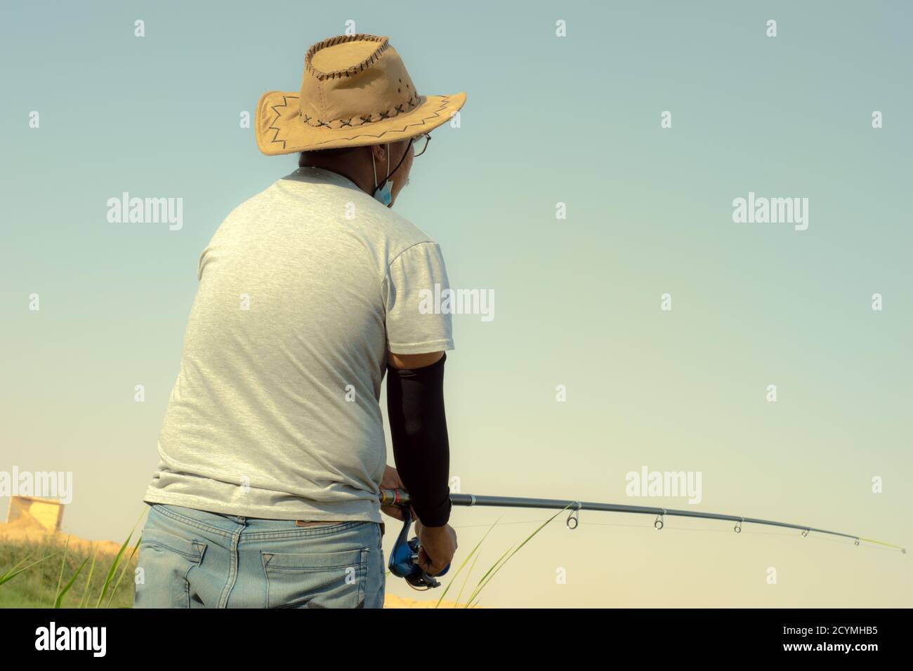 Image of the man in a cowboy hat fishing in the lakeshore Stock Photo