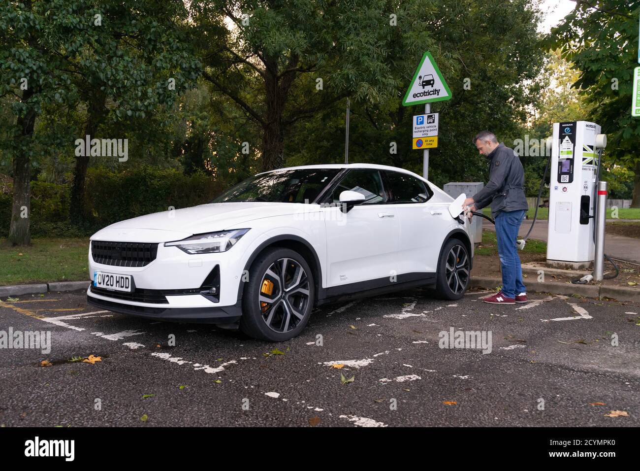 Man charging an electric vehicle in a public EV recharging bay. Vehicle is a Polestar 2 which will soon take on the Tesla Model S Stock Photo