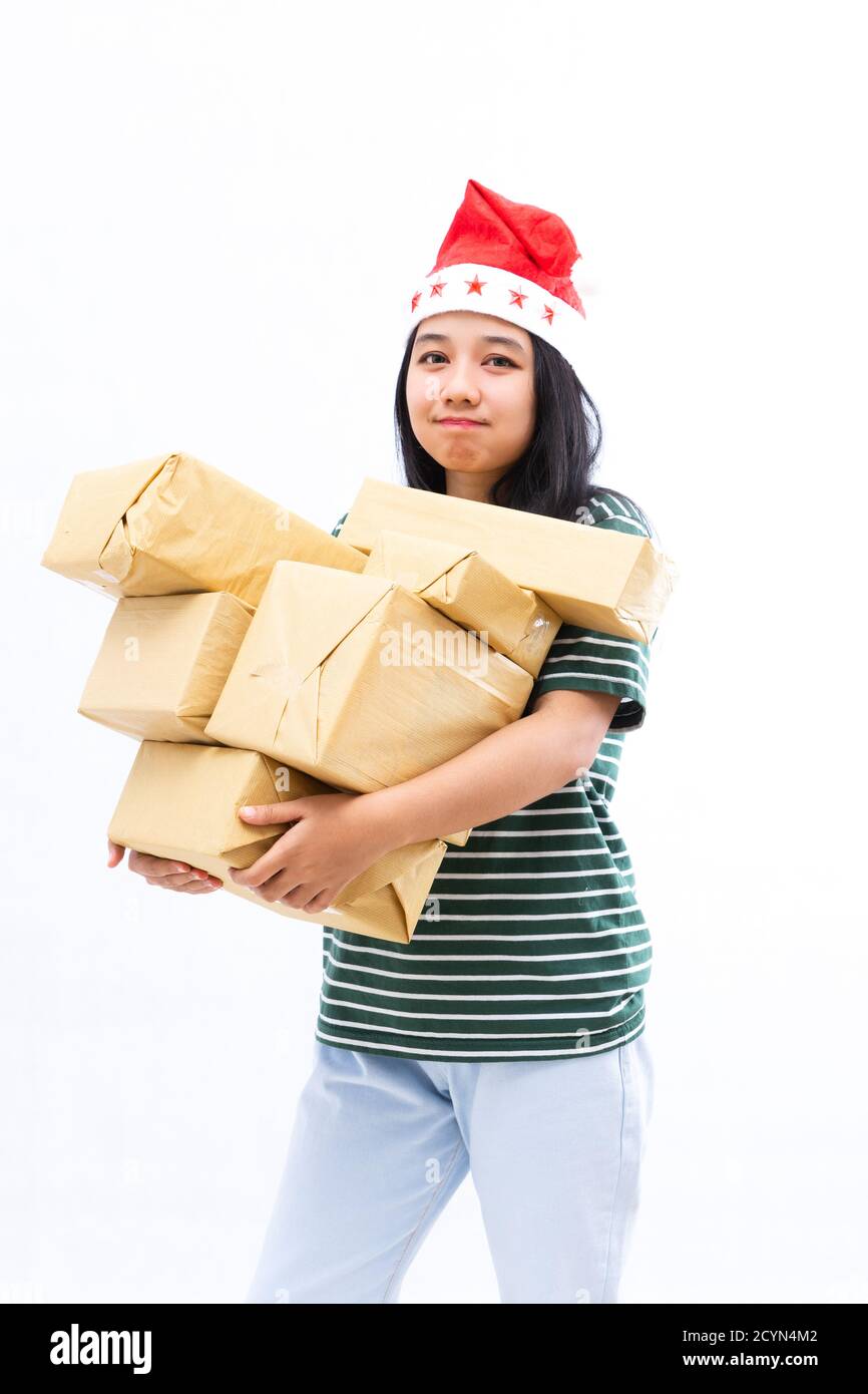 portrait of a young Asian woman wearing a santa hat and wearing casual clothes lifting a pile of gifts with a white isolated background Stock Photo