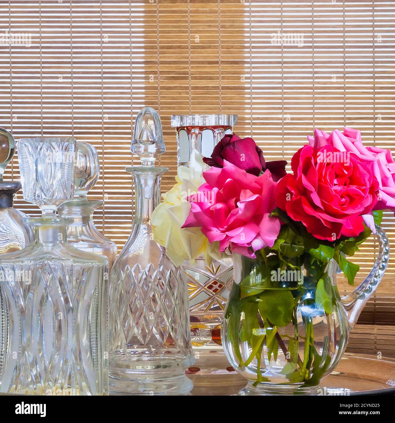 Pink flower in a crystal water jug. Empty vintage crystal decanters on the left. Stock Image Stock Photo