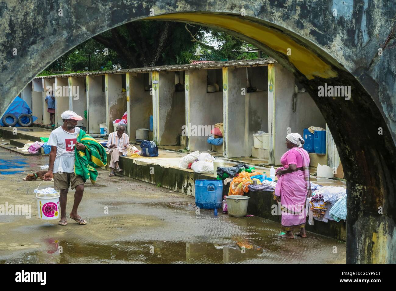 Old lady worker and customers at washing booths in the Dhobi Khana, a rare old Tamil hand wash laundry; Veli, Kochi (Cochin), Kerala, India Stock Photo