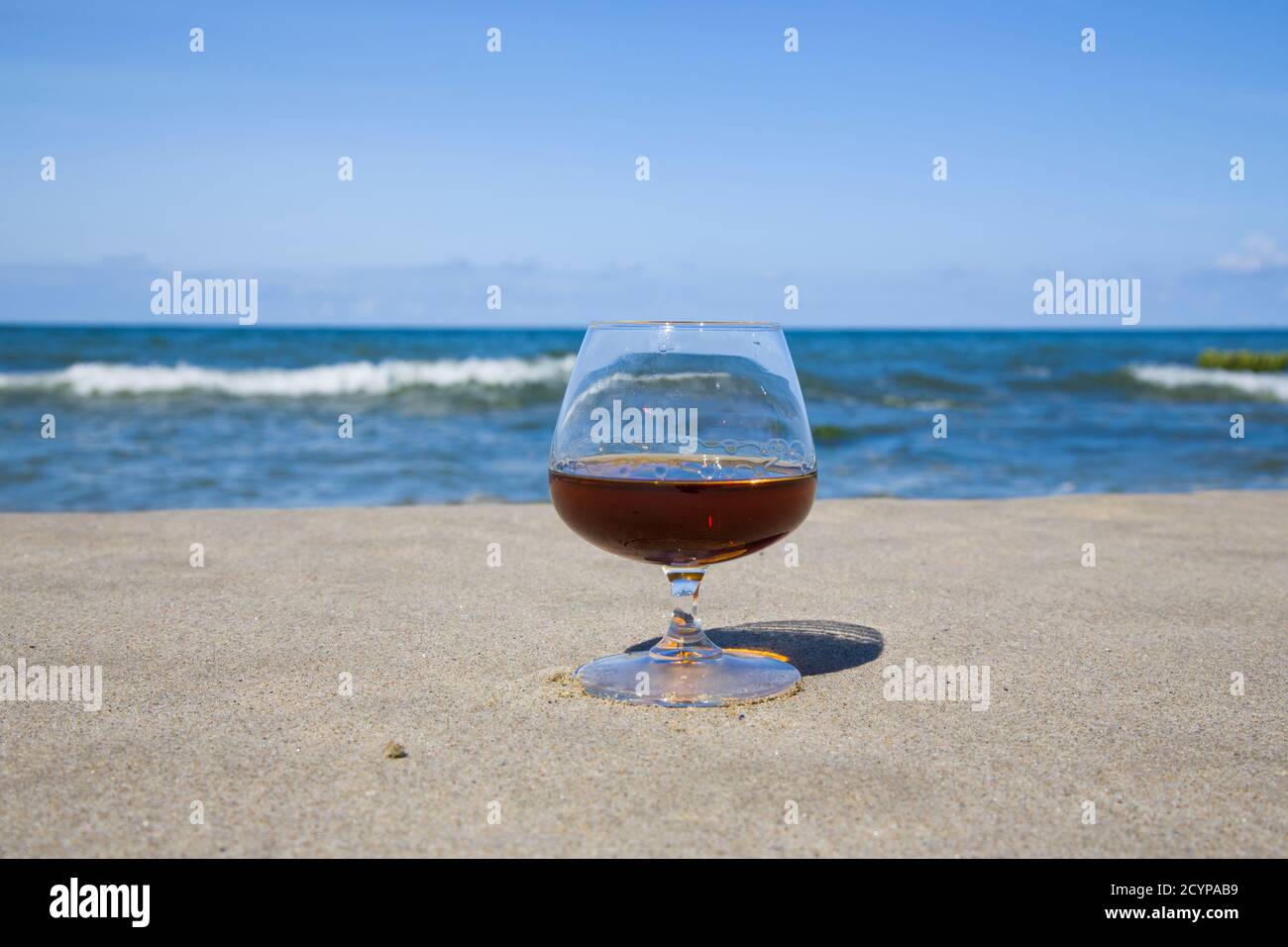 Cognac in a glass on the shore of the blue sea. Stay with alcohol Stock Photo