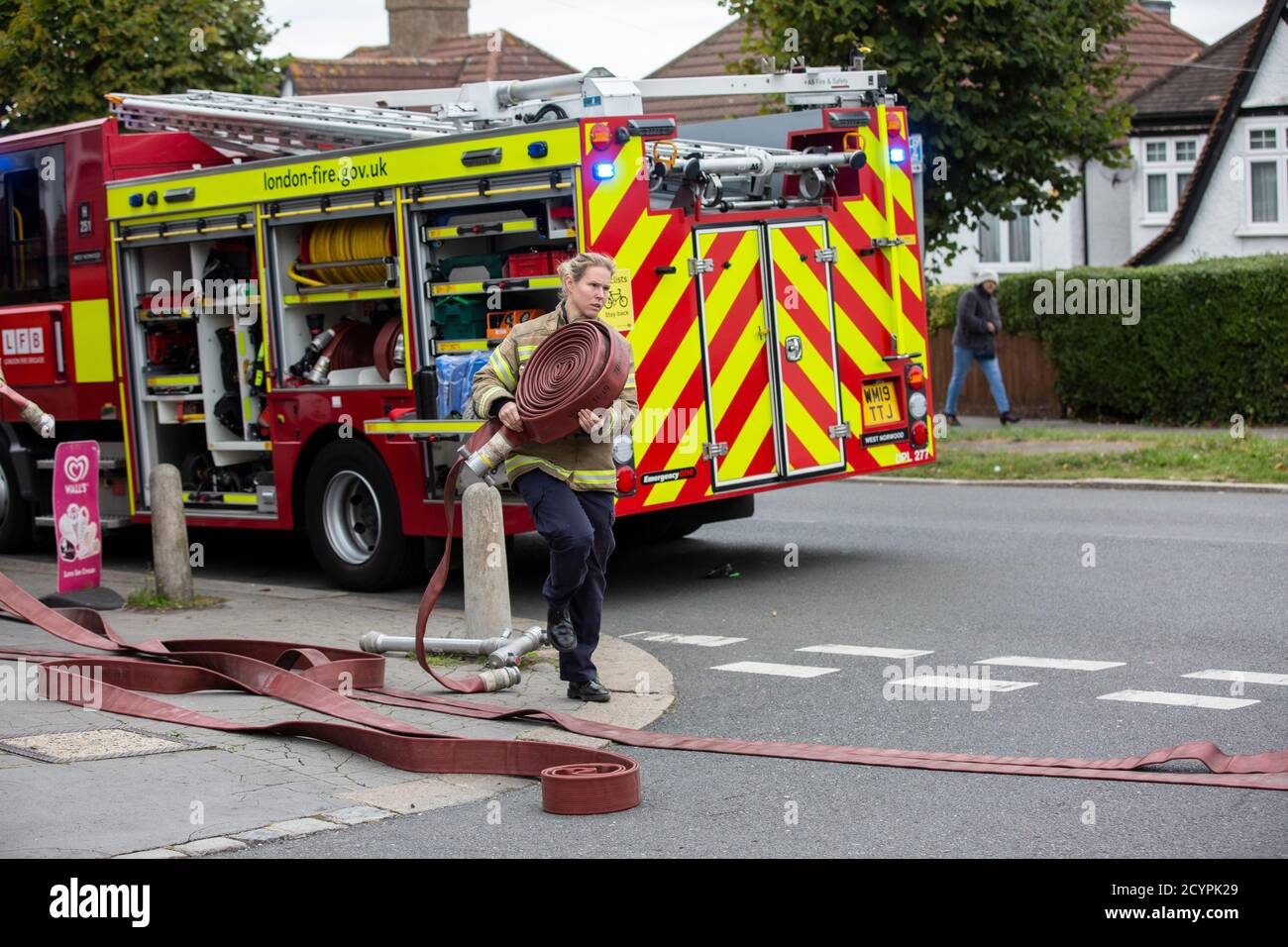 Woman Firefighter rolls out the hose with London Fire Brigade attending a house fire in a residential street, South London, England, United Kingdom Stock Photo