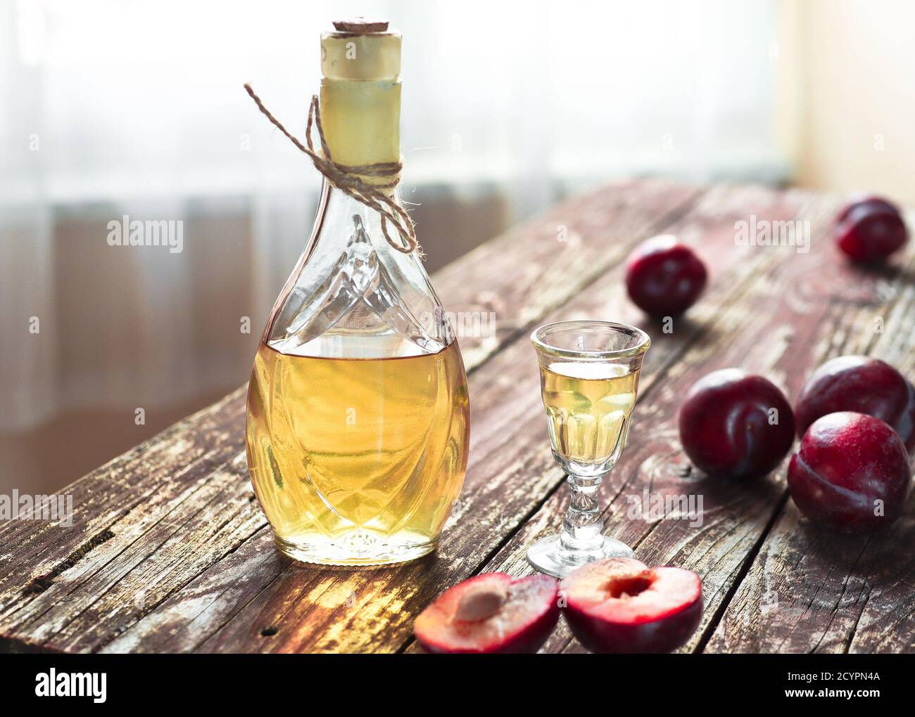 Traditional Balkan plum brandy - rakija or rakia slivovica in the bottle, a wineglass with sljivovica and fresh plums on the wooden background in dayl Stock Photo