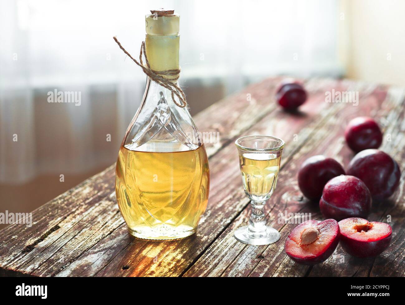 Traditional Balkan plum brandy - rakija or rakia slivovica in the bottle, a wineglass with sljivovica and fresh plums on the wooden background in dayl Stock Photo