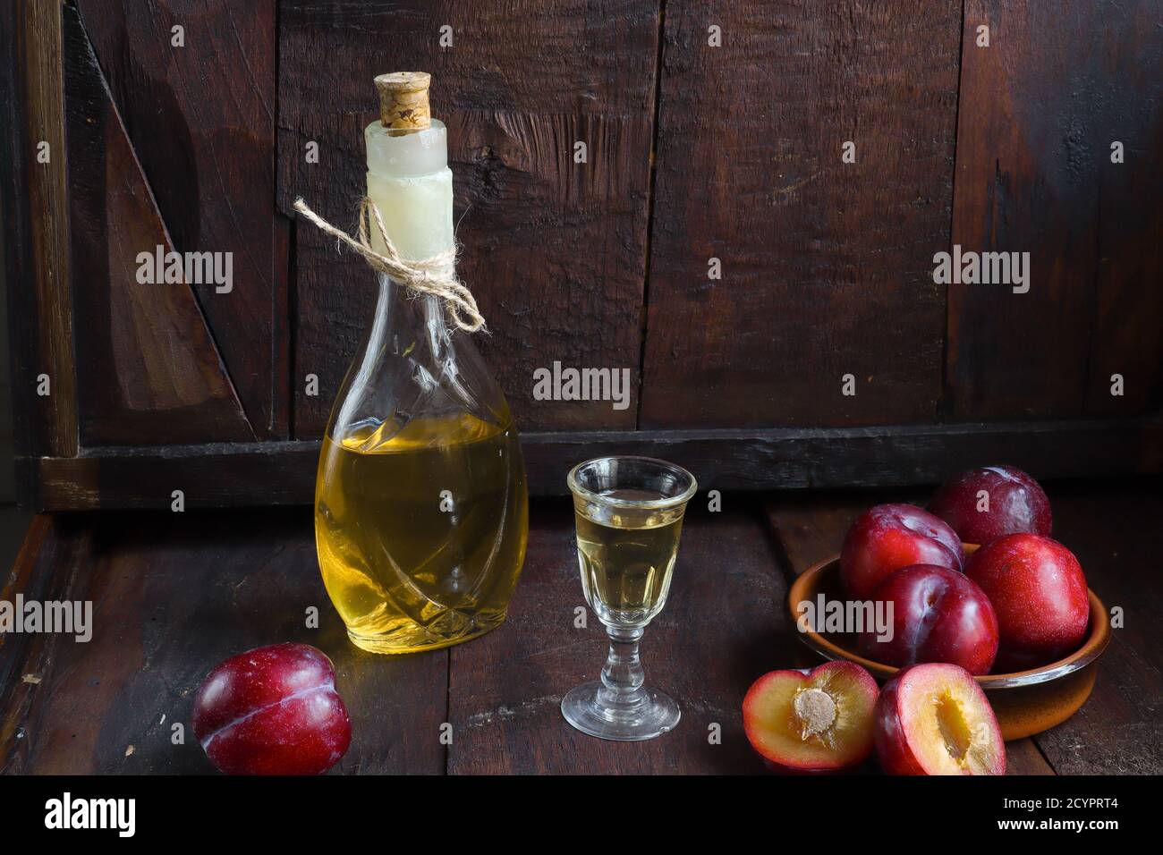 A bottle of rakija or rakia slivovica - traditional Balkan plum brandy near a wineglass with sljivovica and fresh plums on the dark old wooden backgro Stock Photo