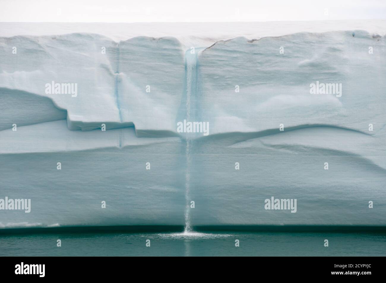 Melting ice water falls from a Northern Arctic glacial wall as a waterfall into a turquoise ocean.Climate Change.Climate Emergency Stock Photo