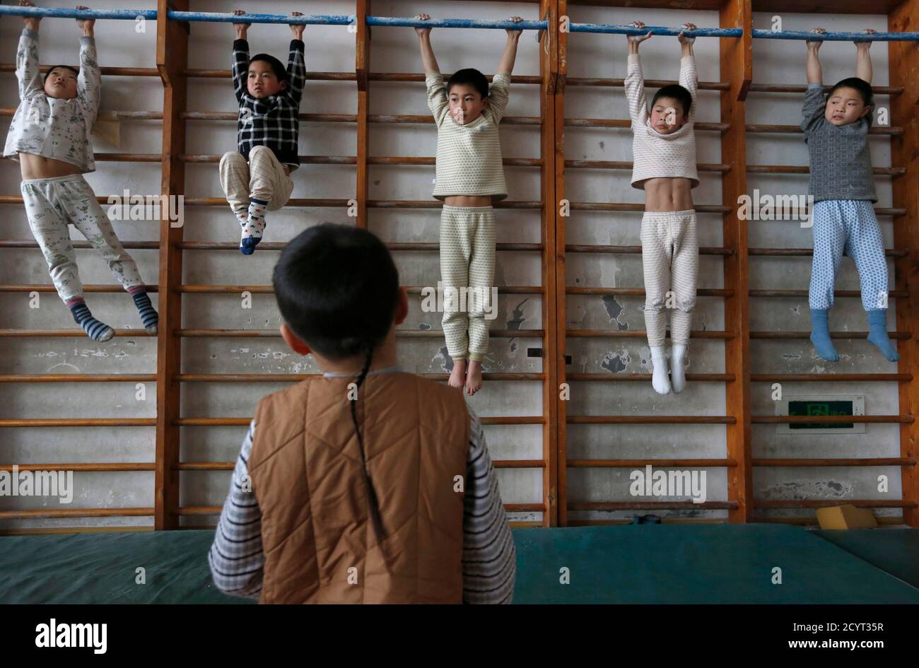 A group of young gymnasts stretch themselves on wooden bars during an exercise session at the gymnastics hall of a sports school in Jiaxing, Zhejiang province, February 28, 2013. Their class consists of children aged six to seven, who have been attending professional sports training for at least four years. Their daily schedule contains literacy and general knowledge classes in the morning and four hours of athletic training in the afternoon. REUTERS/William Hong (CHINA - Tags: SPORT ATHLETICS EDUCATION SOCIETY) Stock Photo